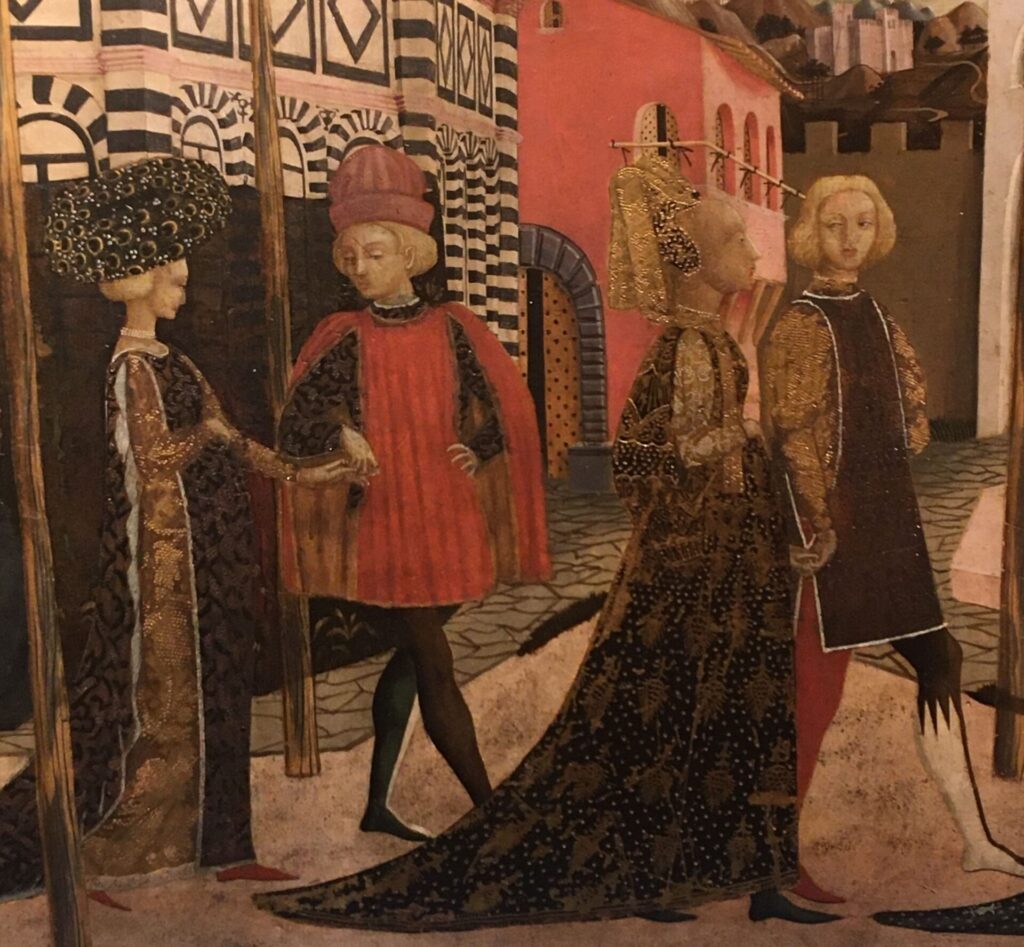 Nella foto un particolare del decoro del Cassone nuziale per una ragazza della famiglia Adimari in mostra alla galleria del’lAccademia di Firenze. Nel particolare due coppie sfilano davanti il battistero che si vede sullo sfondo. I vestiti preziosi in broccato delle dame sono corredati da un fastoso cappello, per una, e una complessa capigliatura per la seconda, testimonianza della moda del tempo