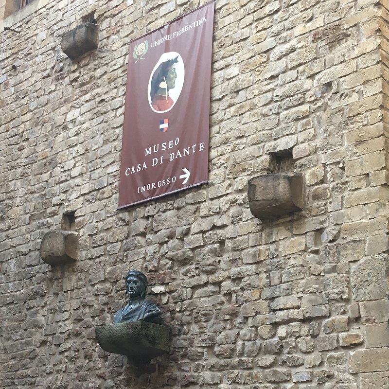 nella foto busto novecentesco di dante alighieri sotto l’insegna che segnala la casa di dante edificata nel punto dove si pensava sorgessero le case torri degli alighieri